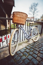 bicycle with a basket leaning against a fence 