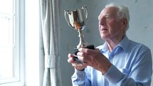 Senior caucasian man cleaning his trophy themes of winning and thinking about past successes
