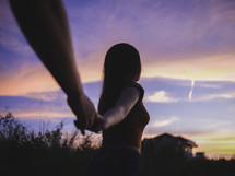 a couple holding hands walking towards a view of the sunset 