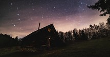 Romantic night sky with milky way stars over old wooden hut in forest nature astronomy timelapse
