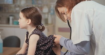 Female doctor examining a little girl's lungs using a stethoscope in the clinic.
