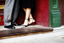 feet of a couple standing in a doorway of city apartment by street heels dress shoes