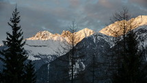 Sunset Evening Colors over Snowy Alps Mountains Time Lapse. Dolly Shot over Trees
