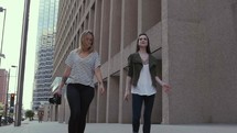 women walking down a downtown sidewalk carrying a camera 
