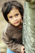 Boy standing behind tree trunk