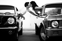 man and a woman leaning out of car windows kissing classic cars ford mustang Chevrolet nova romance