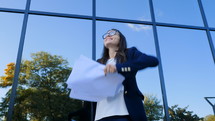 Young businesswoman celebrates success and throwing papers and documents into air on modern office building background. Freedom, successful completion of project concept.