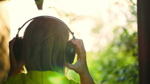 Back shot of a woman putting on the headphones and listening to music enjoying nature scenes