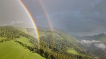 Aerial view of double rainbow moving over green landscape in sunny rainy evening