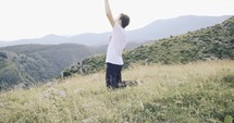 young man kneeling in prayer on a green mountainside 