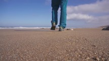Man in blue pants and brown jacket walking on sand beach in sunny ocean coast, low angle view, travel holiday background
