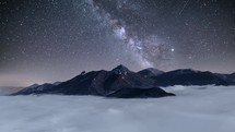 Blue night sky with stars and milky way galaxy move over alpine mountains with foggy clouds in valley Astronomy time lapse
