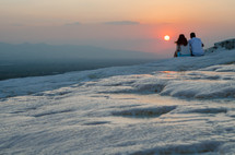 couple sitting on top of Pamukkale (cotton castle) in Turkey, looking out at a sunset 