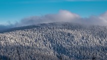 Fast clouds over frozen winter forest mountain in windy evening nature background time lapse
