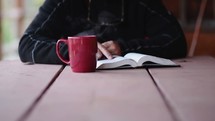 a person sitting reading a Bible with a steaming mug 