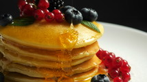 Pancakes with forest berries and honey on white plate and black smoke background. 
