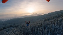 Paragliding flight above winter forest nature at golden sunrise, adrenaline adventure freedom
