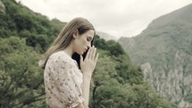 a female with praying hands outdoors 