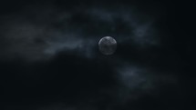 Full moon glowing in the dark covered by black stormy clouds