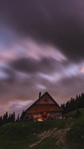 Clouds and milky way galaxy stars moving fast over wooden forest house in summer night
