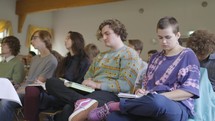 A group of young adults listening to a Bible teaching or sermon with their Bibles open