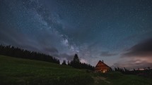 Timelapse sunrise of clouds and milky way galaxy over wooden hut.