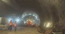 Construction workers supervising heavy machinery during tunnel construction work