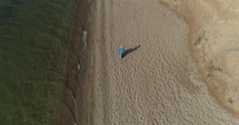 Beautiful girl in a blue dress walks along the sandy beach along the ocean and cliff. Aerial. 