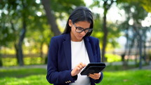Successful business woman with tablet computer on green park background. 