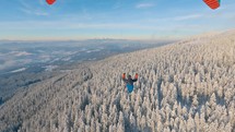 Dreamy paragliding flight above frozen forest mountains nature at magic morning,  adrenaline adevnture freedom, third person view
