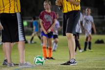 a girl playing soccer standing next to referees 