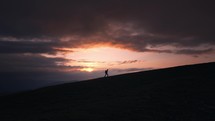 Silhouette of a hiker walking up a hill during sunset