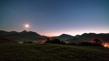 Blue starry night sky with stars and moon light over rural countryside in alpine mountains landscape Astronomy Time lapse