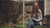 woman sitting on a park bench reading a Bible 