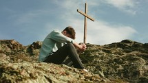 a man praying on a mountainside beside of a cross 