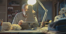 Tracking shot of an senior artist working on sculpturing in clay in a small old studio