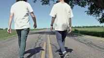 two men walking down the middle of a rural road 