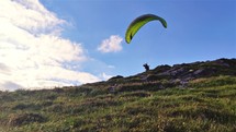 Paraglider on green paragliding wing take off in summer mountain adrenaline adventure 
