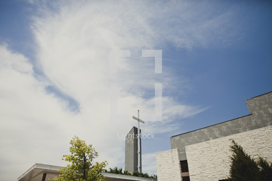 A cross stands high atop a church building.