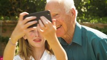 Senior man and his Grand Daughter taking selfies with a smart phone themes of selfie communication togetherness technology