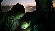 Tilt shot of mother and son using tablet computer while traveling on backseat of a car at night