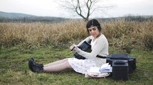 a young woman sitting on a mountainside with her guitar writing music 