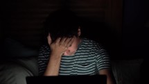 a stressed man looking at his computer screen and covering his face with his hands 