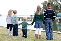 Five children holding hands while looking at a lake.