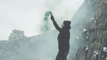 a man standing outdoors holding a smoke flare 