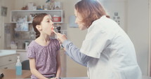 Female doctor checking a young girl's throat using a otoscope in the clinic.