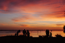 Silhouettes of people on the beach looking at a colorful sunset.