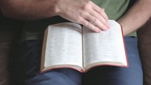 Man's hands turning pages of the Bible.
