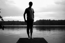 Silhouette of a man standing on a pier on a lake.