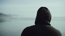 a man walking on a beach in a hoodie with his back to the camera 